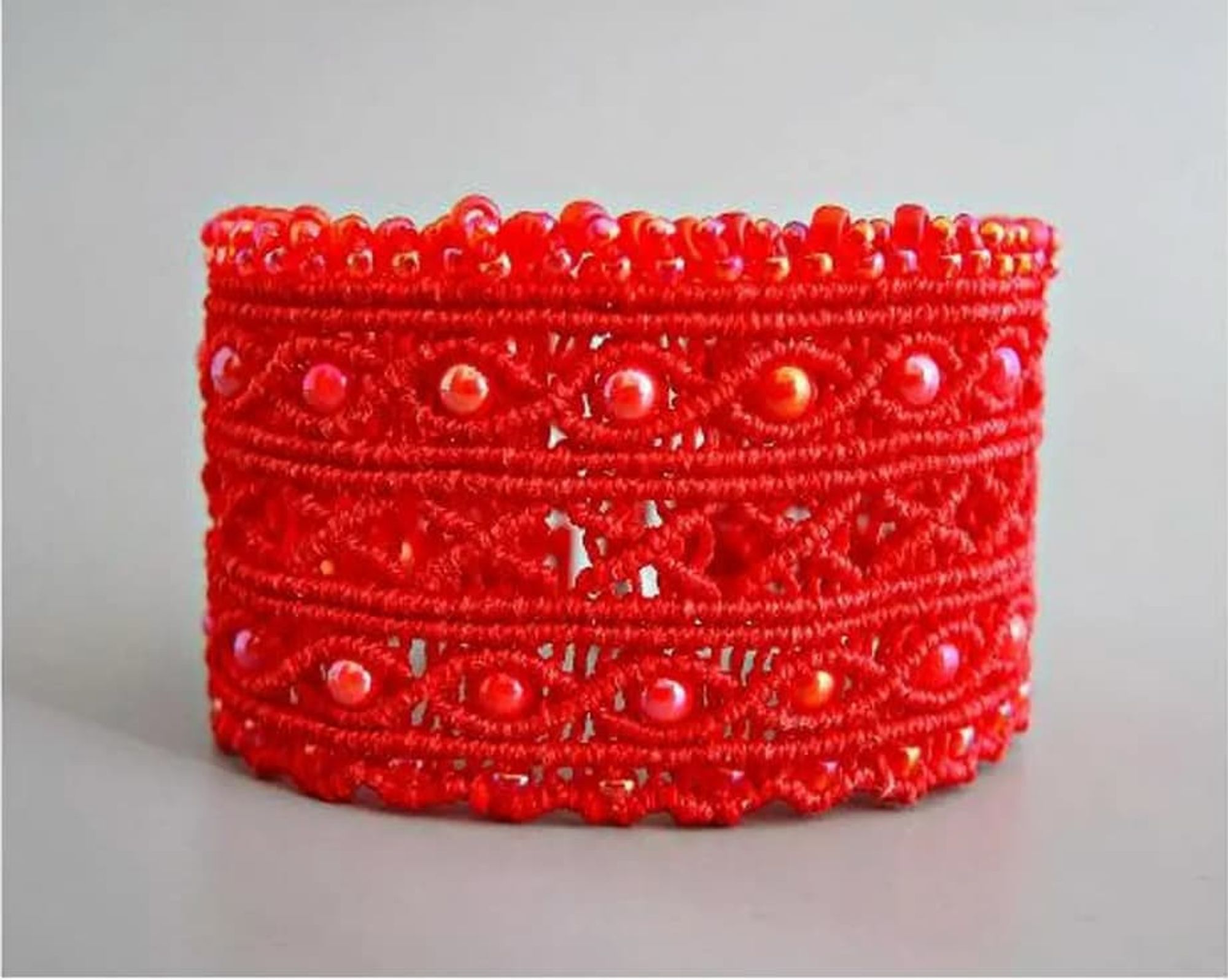 red beaded micro macrame cuff laying on a desk